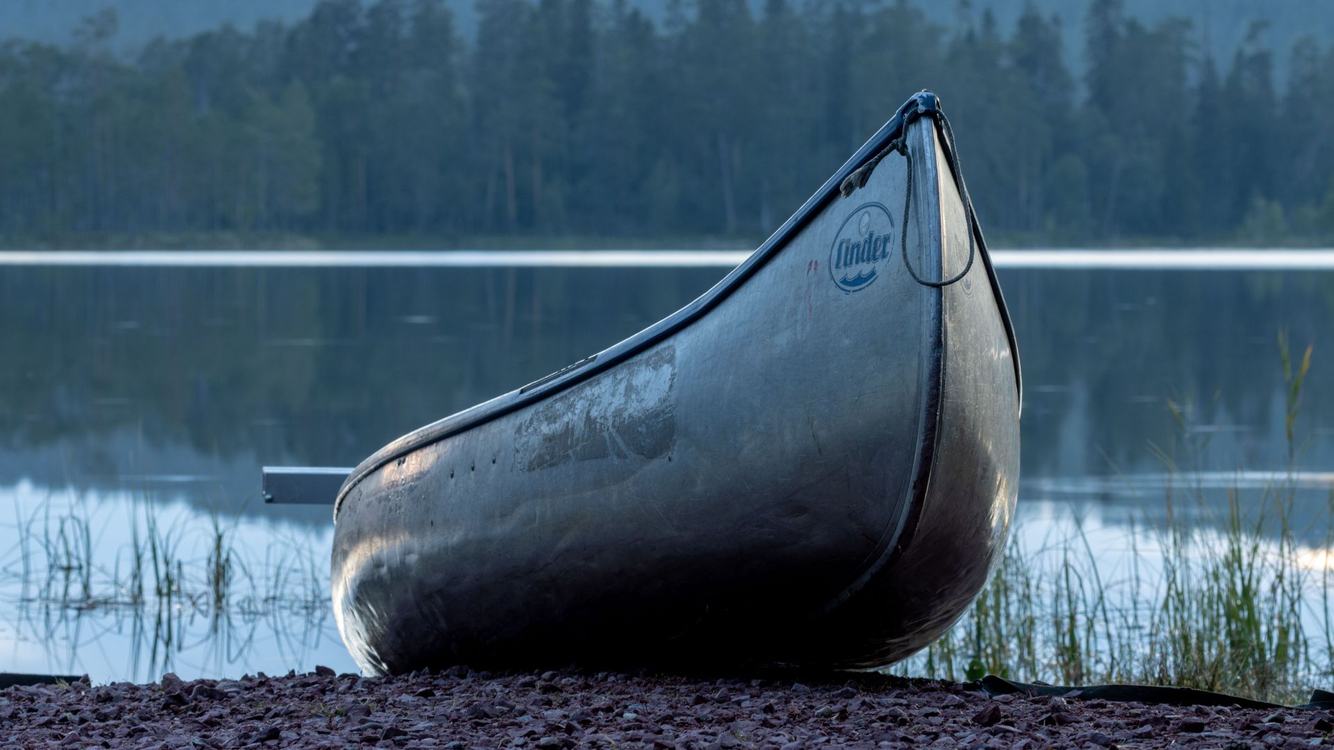 A weathered canoe resting at the shoreline of Lake Rensjön in Dalarna, Sweden, after an evening fishing trip. Calm water and a forested shoreline give the scene a quiet, settled…