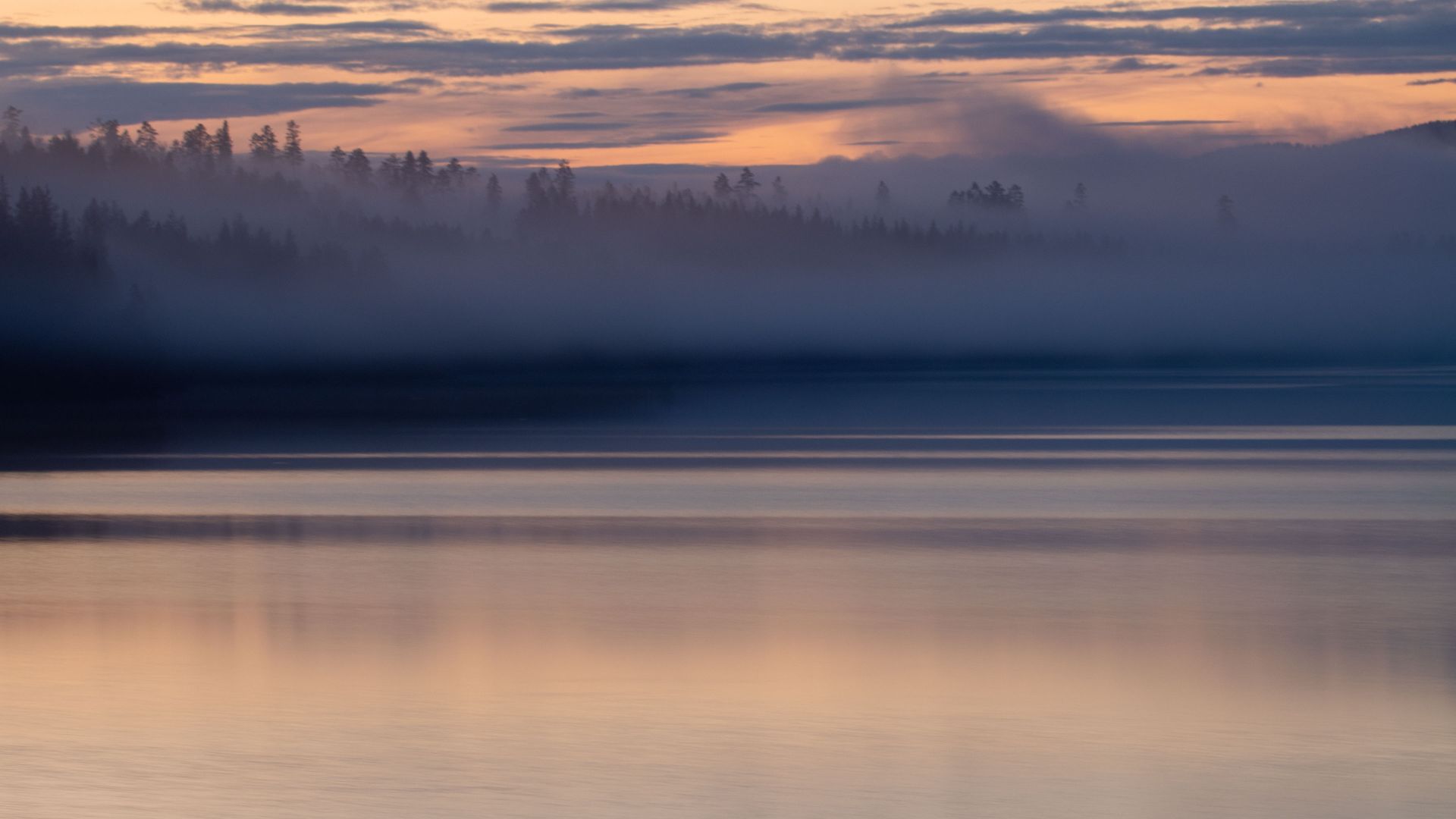 Late evening light over Trängslet Reservoir in Dalarna, Sweden, with mist drifting across the water and forested hills silhouetted beneath a warm summer sky.